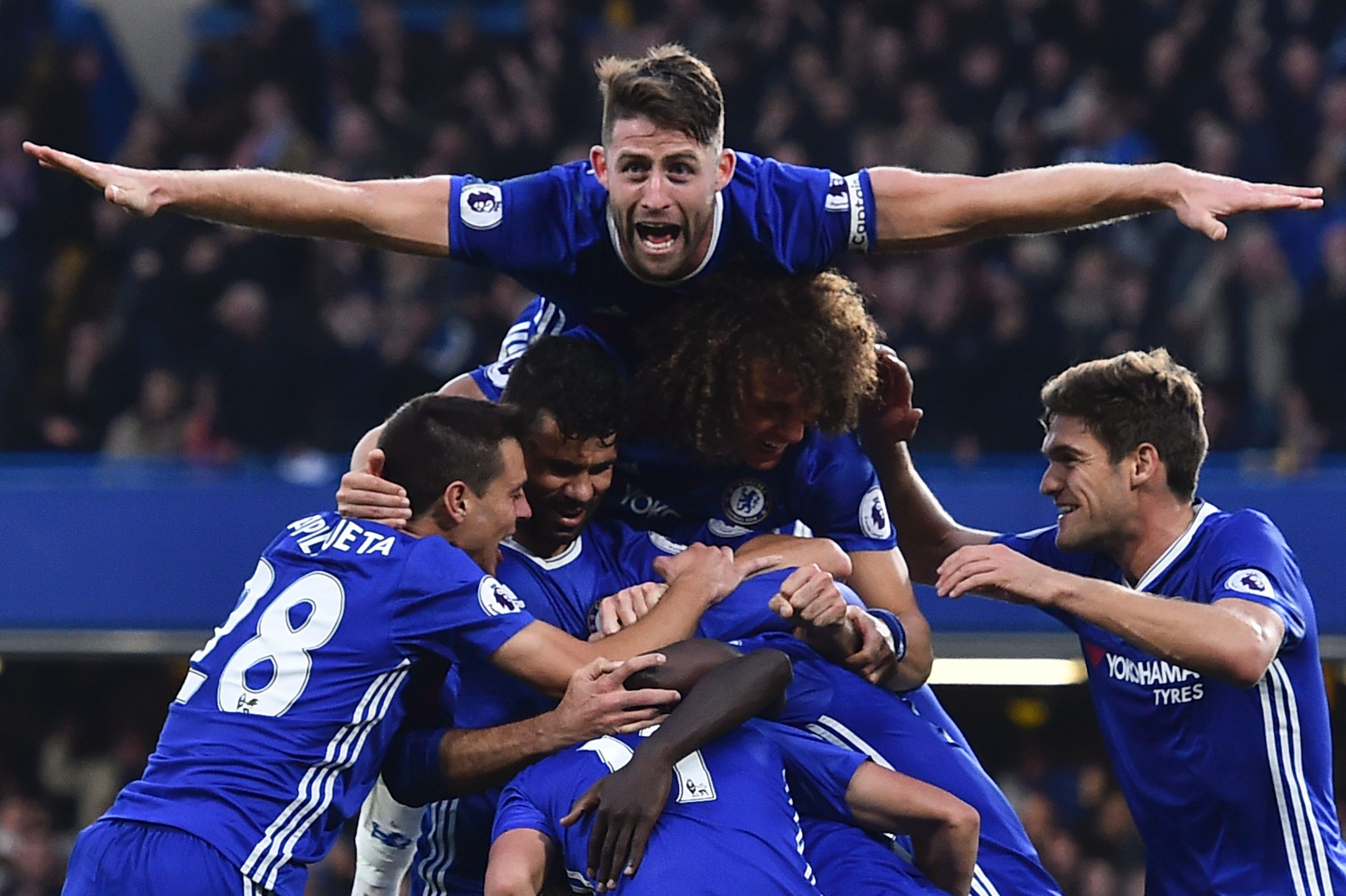 Chelsea's English defender Gary Cahill (top) jumps onto the huddle to join the celebrates after Chelsea's French midfielder N'Golo Kante scored their fourth goal during the English Premier League football match between Chelsea and Manchester United at Stamford Bridge in London on October 23, 2016. / AFP / GLYN KIRK / RESTRICTED TO EDITORIAL USE. No use with unauthorized audio, video, data, fixture lists, club/league logos or 'live' services. Online in-match use limited to 75 images, no video emulation. No use in betting, games or single club/league/player publications.  /         (Photo credit should read GLYN KIRK/AFP/Getty Images)