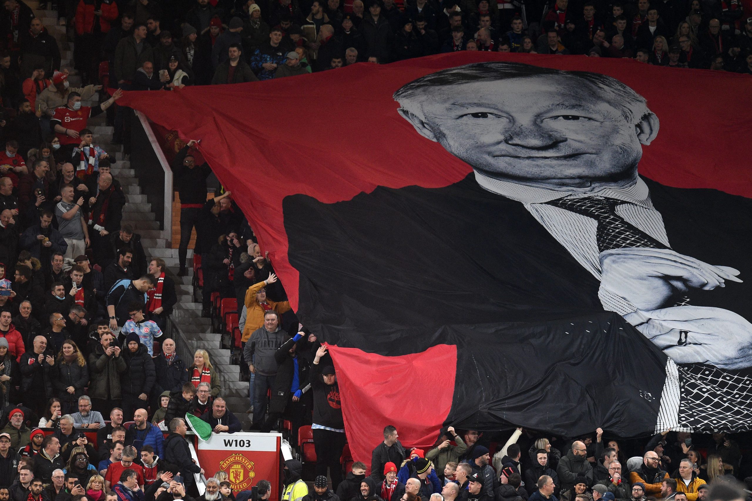 A large banner showing former manager Alex Ferguson is unfurled to celebrate his 80th birthday ahead of the English Premier League football match between Manchester United and Burnley at Old Trafford in Manchester, north-west England, on December 30, 2021. - RESTRICTED TO EDITORIAL USE. No use with unauthorized audio, video, data, fixture lists, club/league logos or 'live' services. Online in-match use limited to 120 images. An additional 40 images may be used in extra time. No video emulation. Social media in-match use limited to 120 images. An additional 40 images may be used in extra time. No use in betting publications, games or single club/league/player publications. (Photo by Oli SCARFF / AFP) / RESTRICTED TO EDITORIAL USE. No use with unauthorized audio, video, data, fixture lists, club/league logos or 'live' services. Online in-match use limited to 120 images. An additional 40 images may be used in extra time. No video emulation. Social media in-match use limited to 120 images. An additional 40 images may be used in extra time. No use in betting publications, games or single club/league/player publications. / RESTRICTED TO EDITORIAL USE. No use with unauthorized audio, video, data, fixture lists, club/league logos or 'live' services. Online in-match use limited to 120 images. An additional 40 images may be used in extra time. No video emulation. Social media in-match use limited to 120 images. An additional 40 images may be used in extra time. No use in betting publications, games or single club/league/player publications. (Photo by OLI SCARFF/AFP via Getty Images)